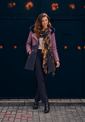 Woman wearing a mustard and navy quilted coat with dark trousers and a lightweight scarf with a navy and mustard print
