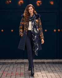 Woman wearing a dusty rose and navy quilted coat with dark trousers and a lightweight scarf with a navy and white print